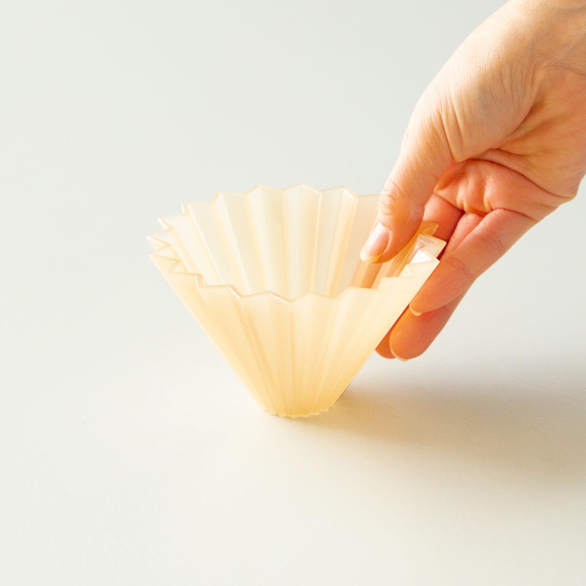 Der Origami Air Dripper in der Farbe Beige von vorne gehalten von einer Hand.